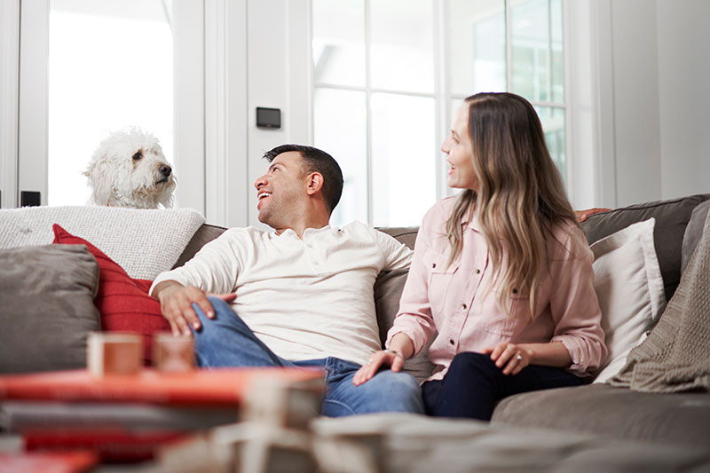 Couple smiling at their dog that's popped up behind the couch